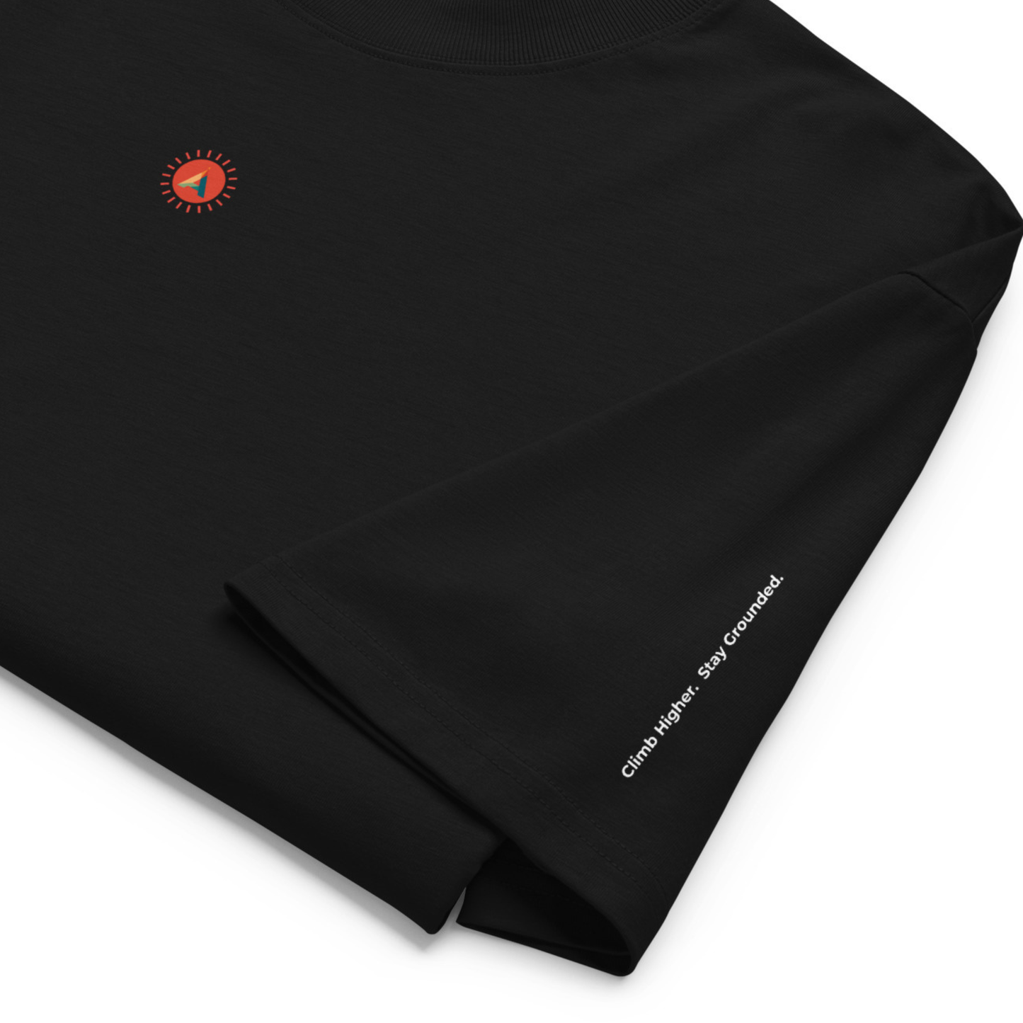 Close-up of the black Aether Peak oversized organic cotton t-shirt with subtle sunburst chest logo and “Climb Higher. Stay Grounded.” sleeve detail.