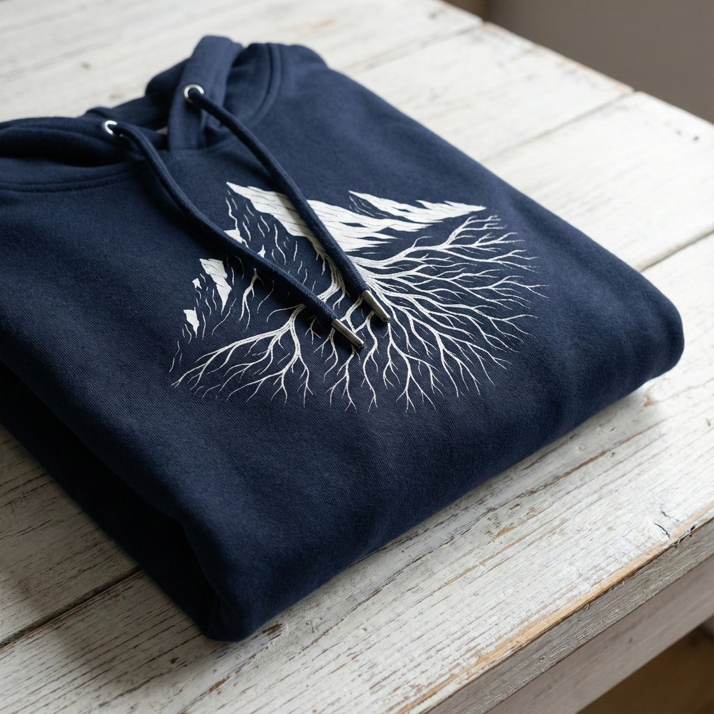 Folded French Navy hoodie with white Mountain Roots design on a white wooden table