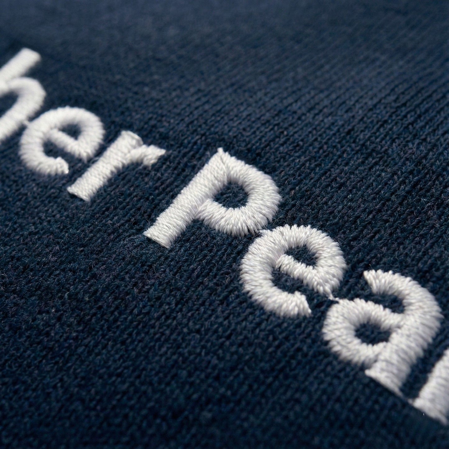 Close-up of embroidered Aether Peak logo on a French Navy Organic cotton fabric.