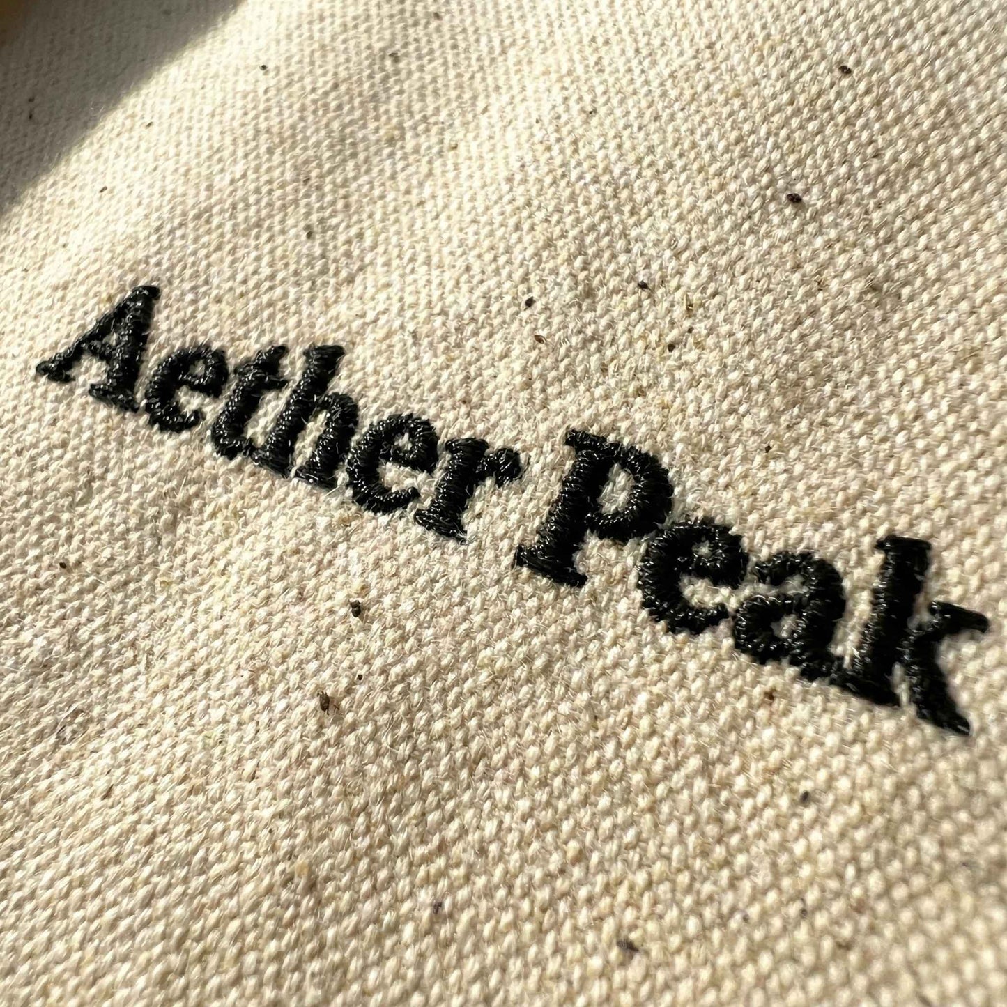 Close-up of black “Aether Peak” embroidery on desert dust organic twill fabric.