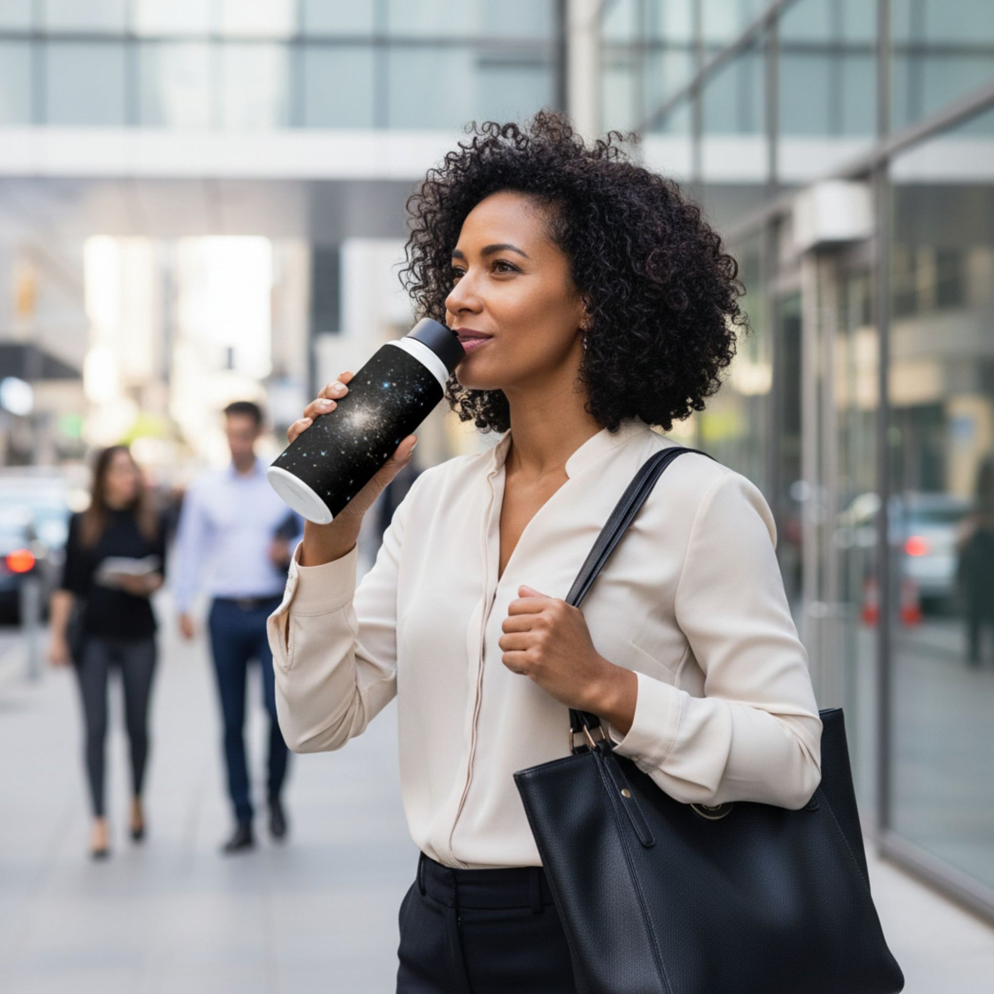 A woman holding a black starry sky stainless steel water bottle and a black handbag in an urban setting