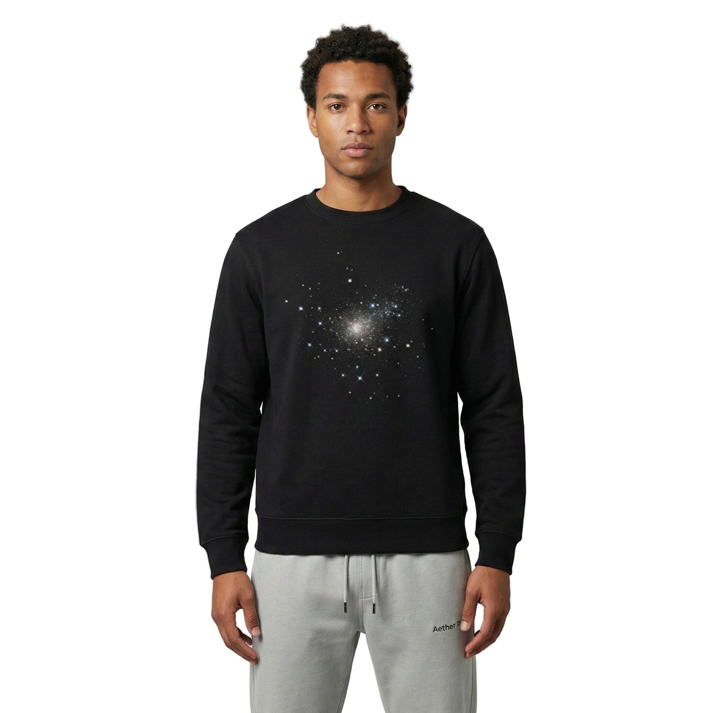 Man wearing a black Aether Peak Starry Sky eco sweatshirt with galaxy print, standing in a minimal studio setting with light grey joggers.
