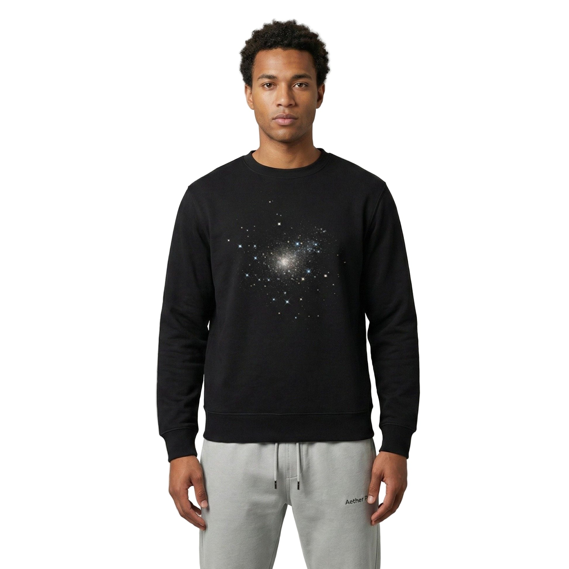 Man wearing a black Aether Peak Starry Sky eco sweatshirt with galaxy print, standing in a minimal studio setting with light grey joggers.
