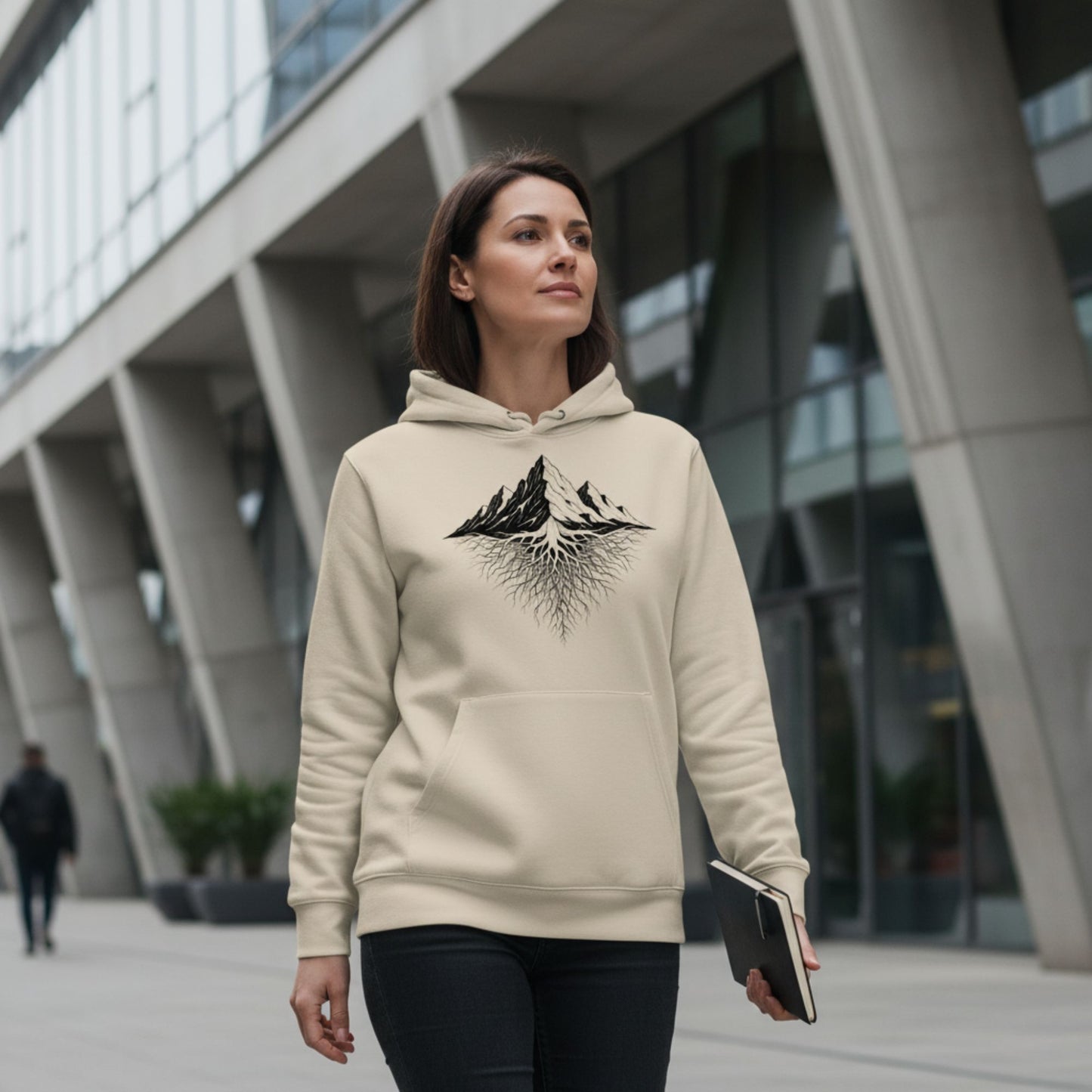 A Woman wearing a Desert Dust hoodie with a mountain roots design, walking in an urban setting.