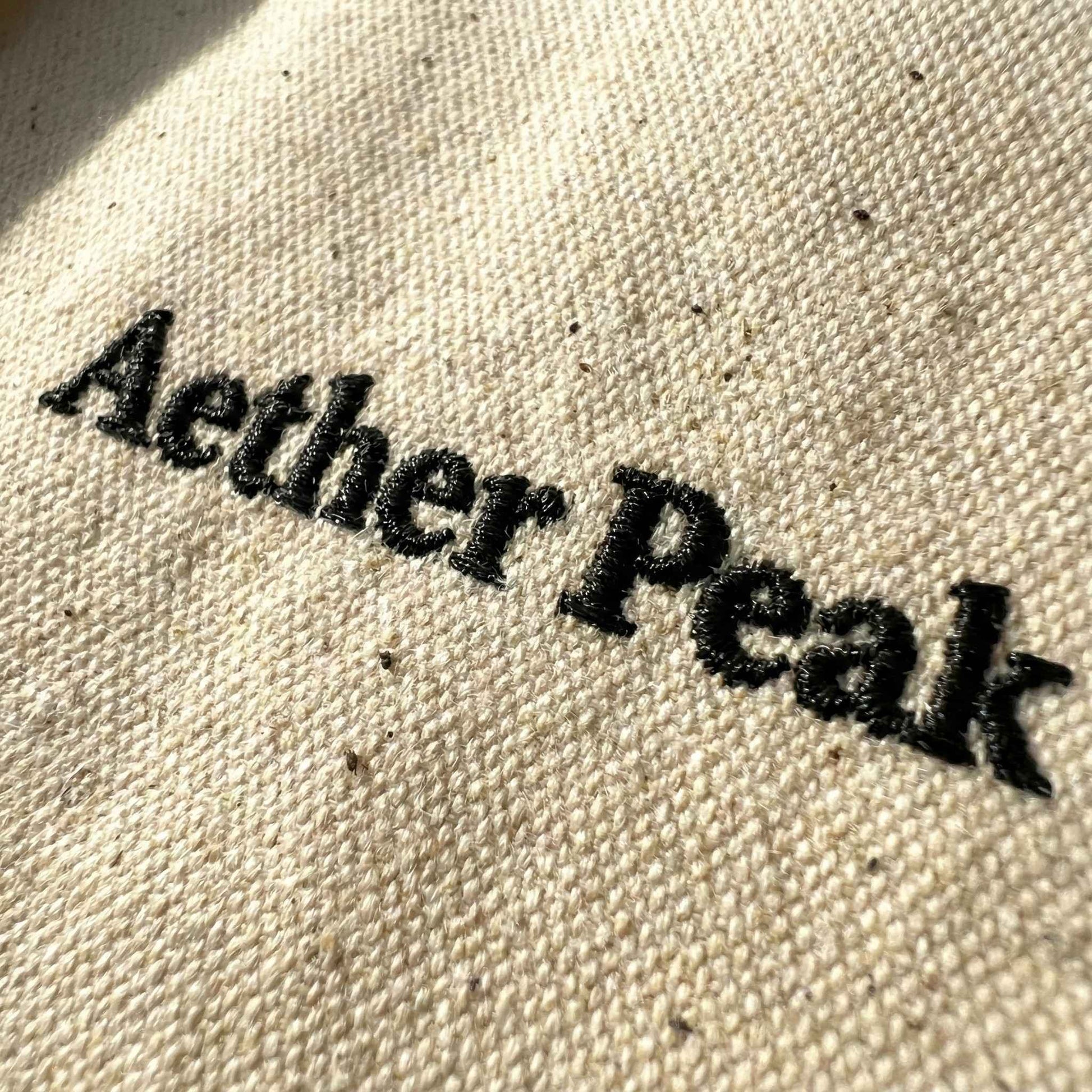 Close-up of black “Aether Peak” embroidery on desert dust organic twill fabric.