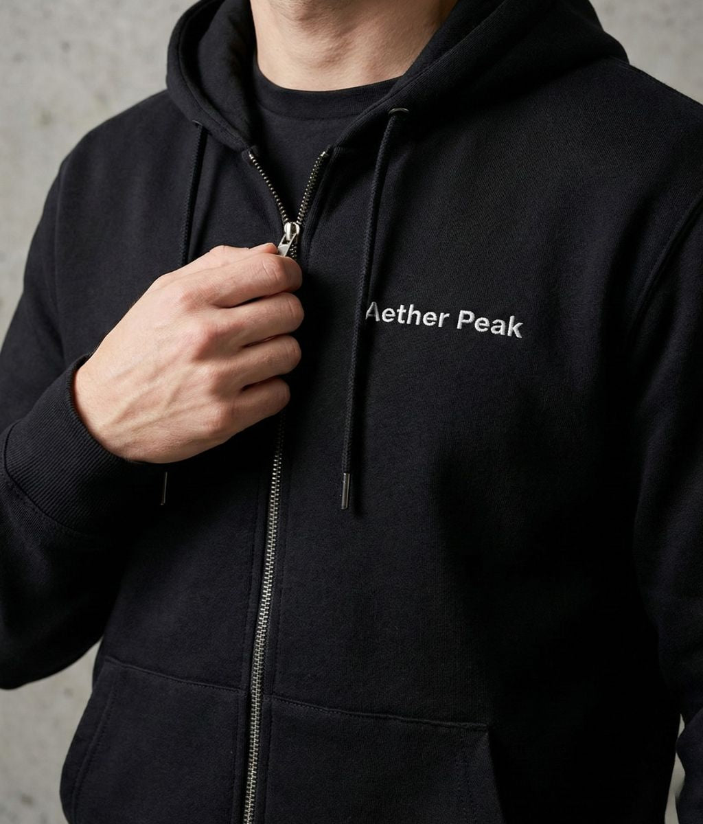 Close-up of black Aether Peak organic zipped hoodie with logo and metal zip detail.